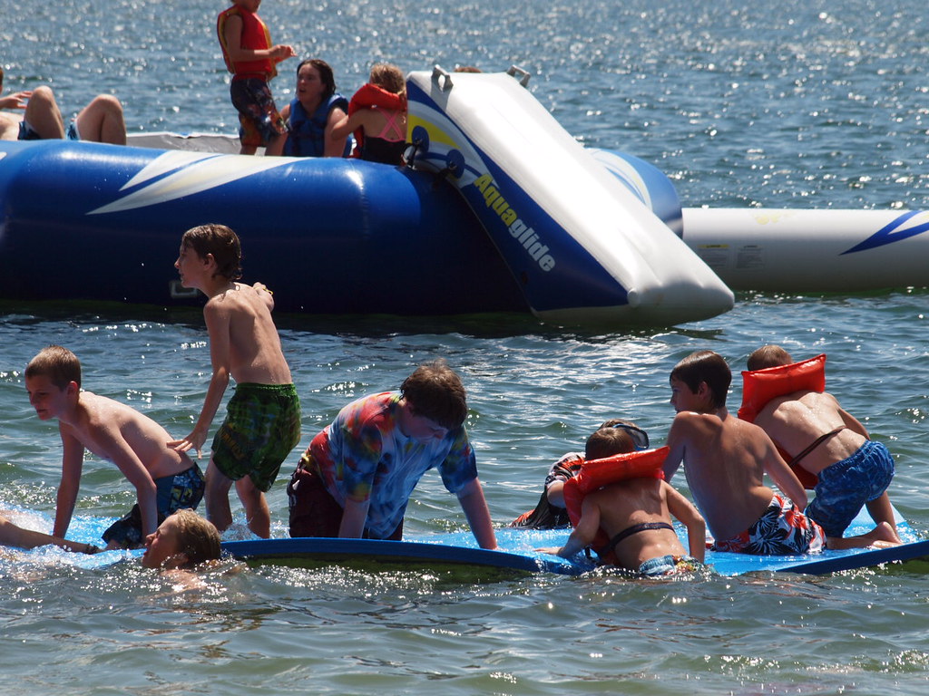 Children playing in the water. Some are on rafts and some are wearing lifejackets. 