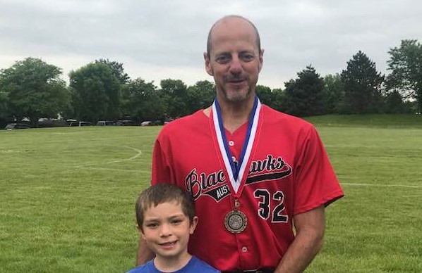 Photo of Michael Finn wearing a gold medal. A child is also standing by him. 
