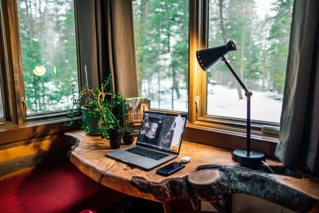 Photo of home office with a wood desk facing the window with a laptop and cellphone. 