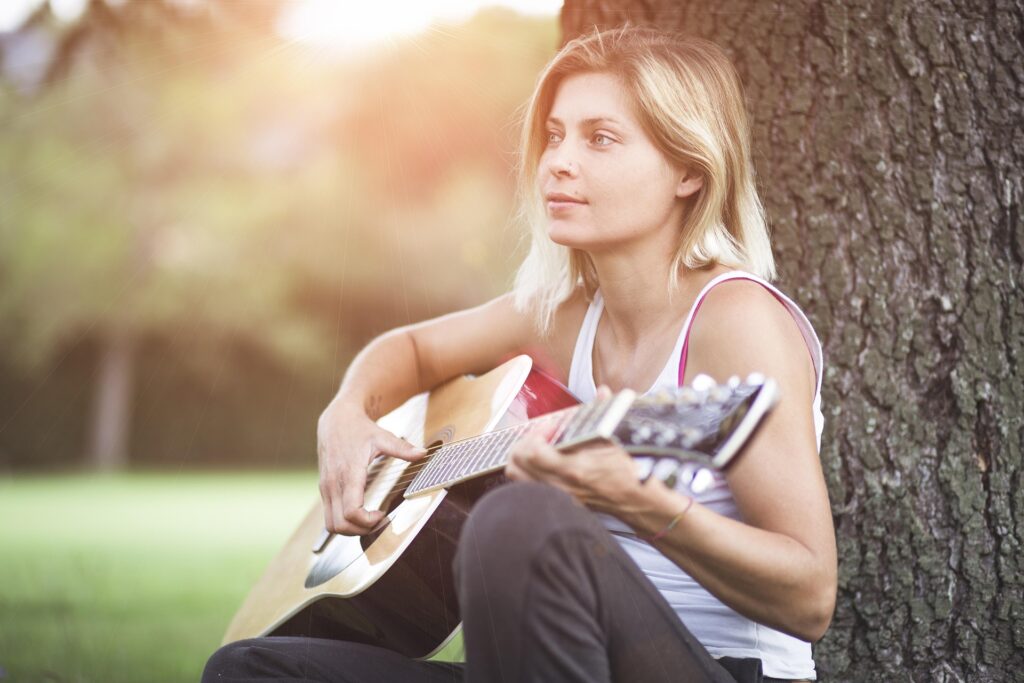 Young adult leans against a tree and strums guitar