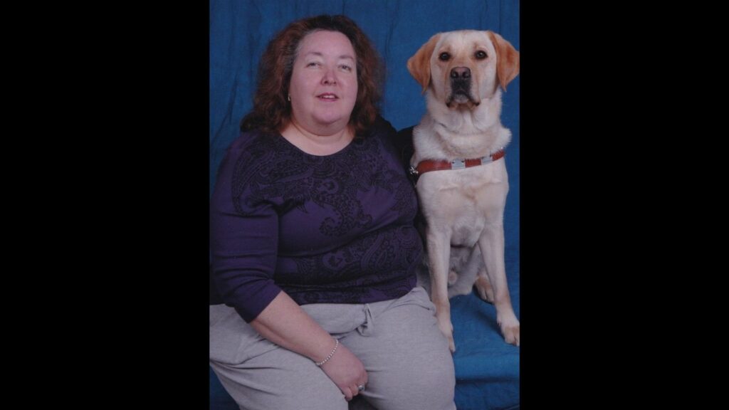 Person sitting for a professional photo with a dog guide in harness.