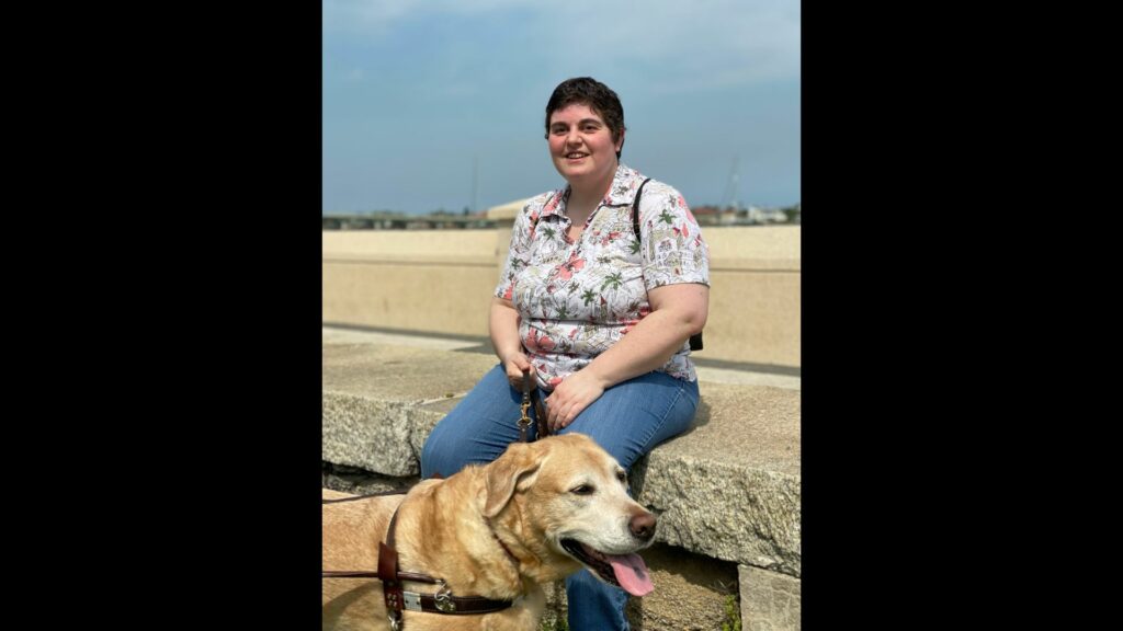 Individual sits outside with backpack and a dog guide