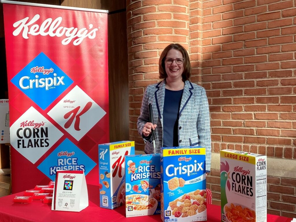 Individual holding a white cane stands behind a table showcasing Kellogg’s cereals.